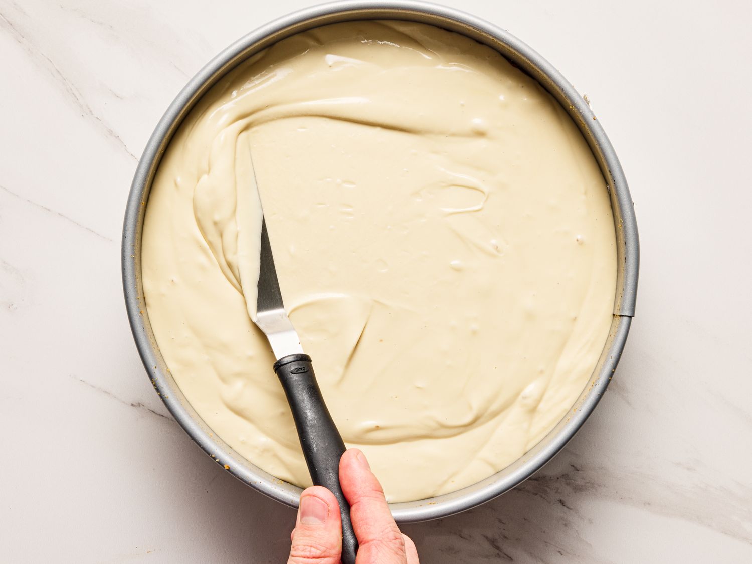 A person smoothing batter in a round pan with an offset spatula