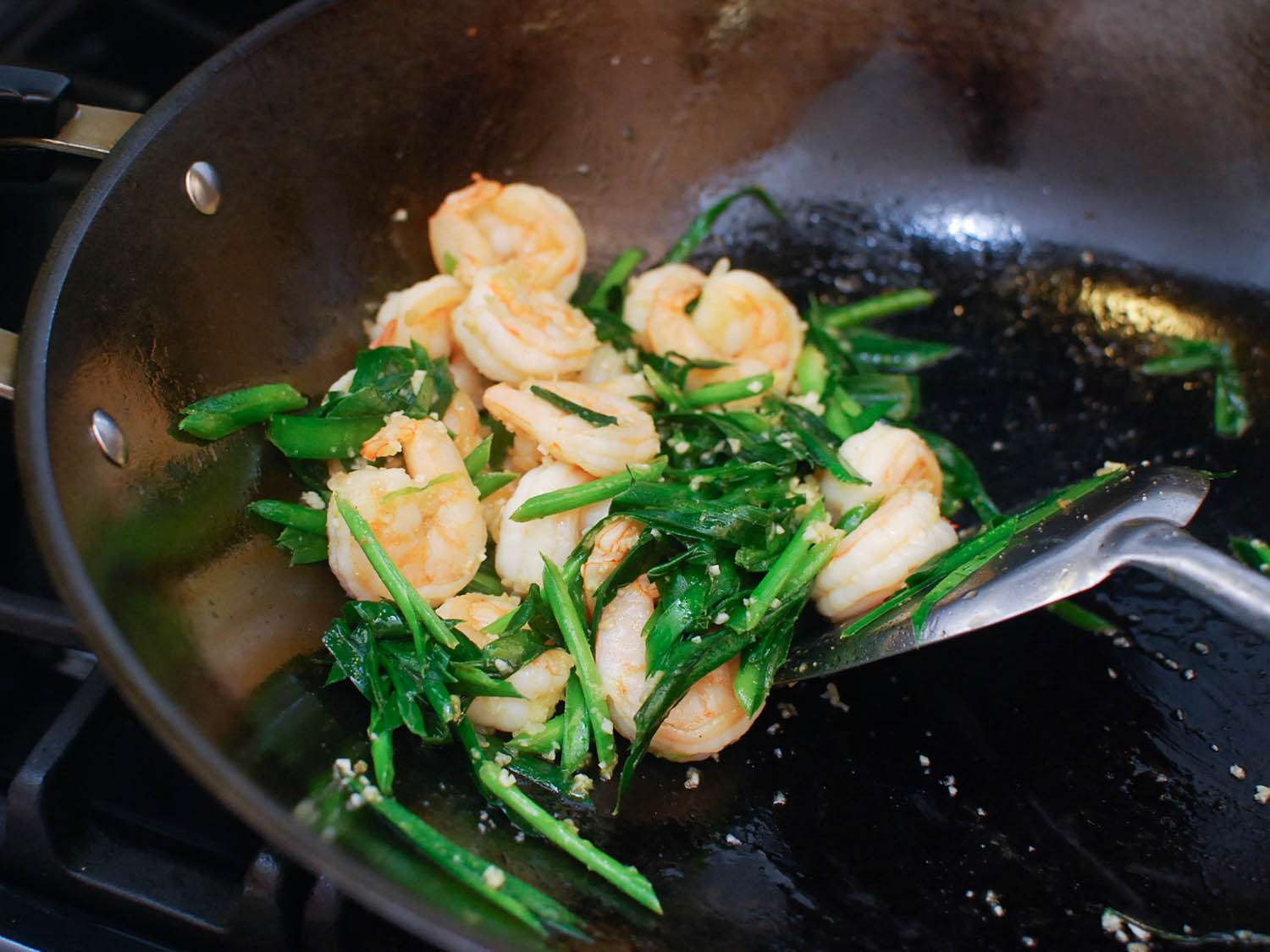 Shrimp and chives are stir-fried on a wok.