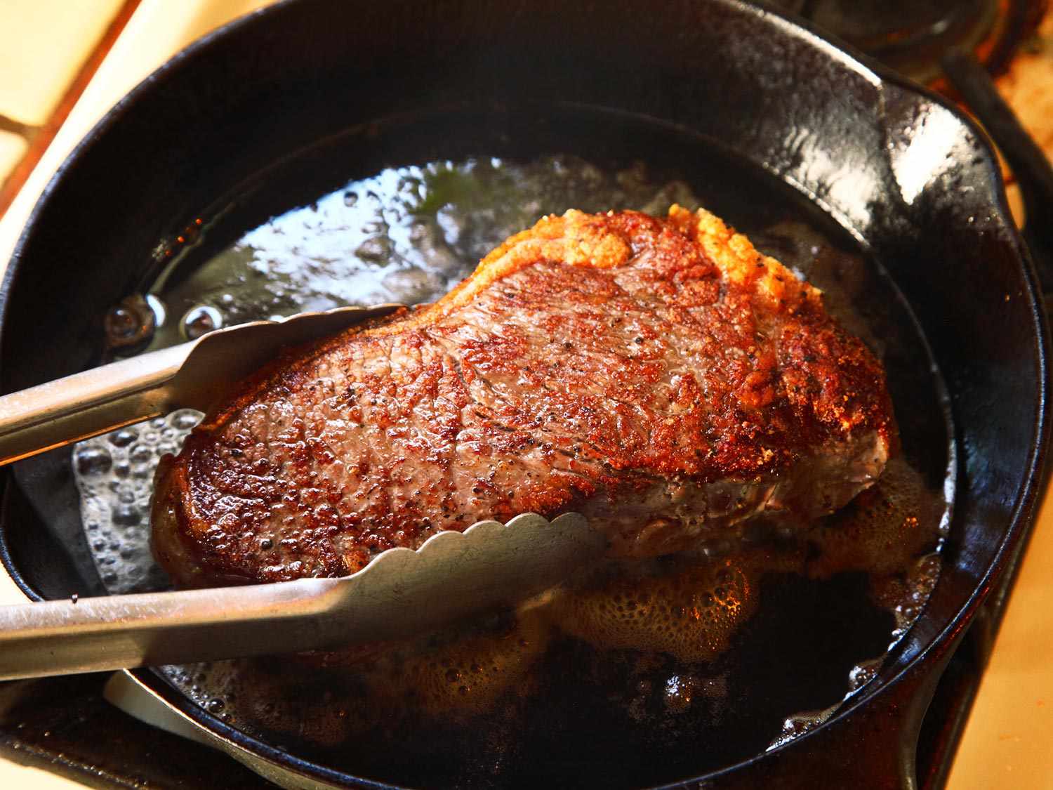A steak being seared in a cast iron pan, demonstrating heat through conduction.