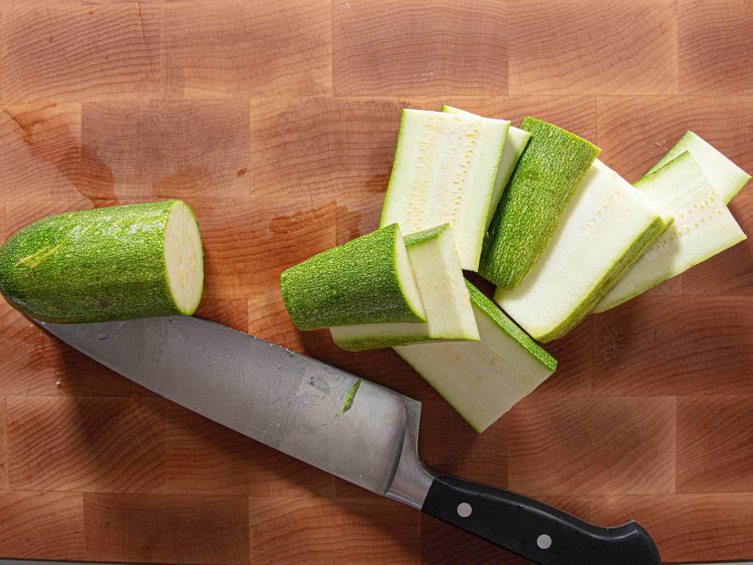 Chopped zucchini pieces and a knife on a cutting board