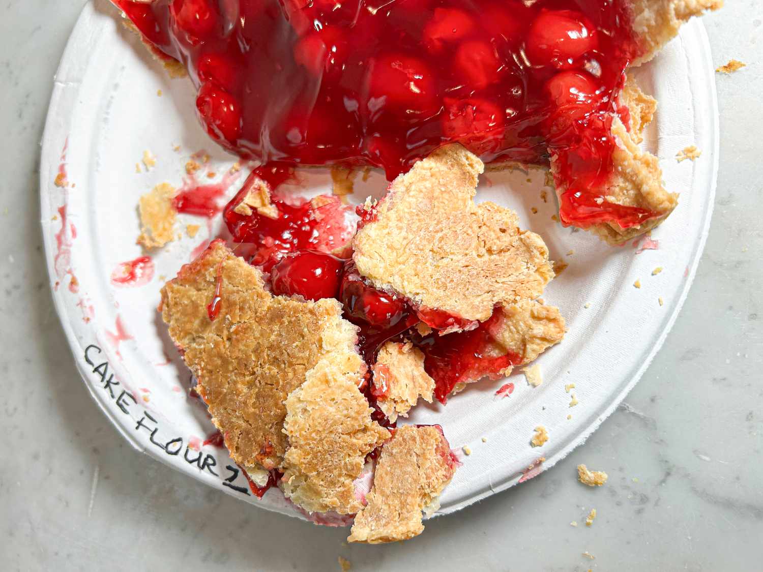 Cherry pie slice on a plate labeled Cake Flour 2 with crust and filling exposed