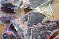 Various packaged cuts of Omaha Steaks meat arranged on a surface including a hand holding one package