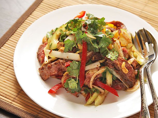 A white dish of steak salad with cucumbers, red peppers, and spicy fish sauce vinaigrette