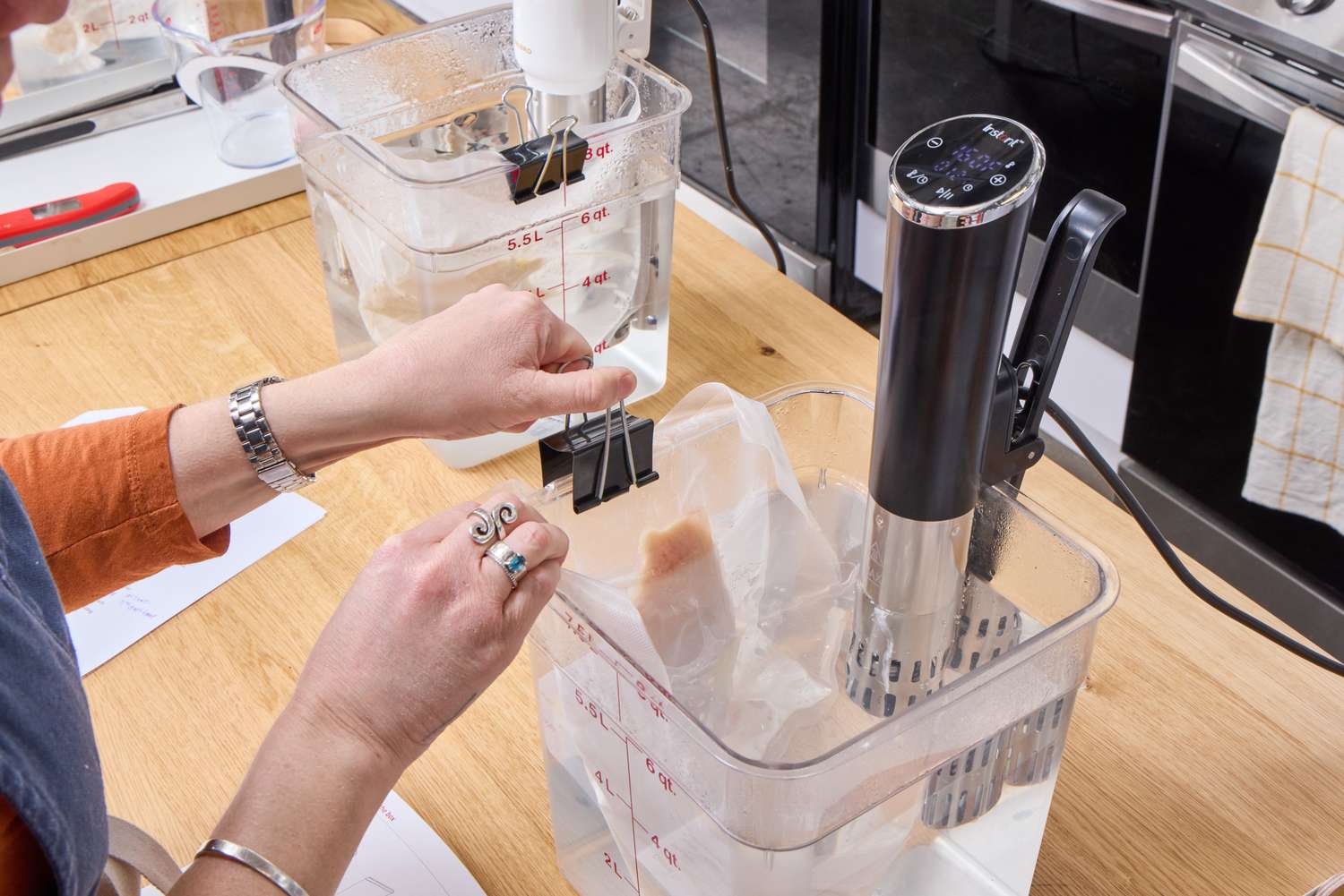 A person secures a sealed bag to the side of a container holding the Instant Accu Slim Sous Vide Immersion Circulator