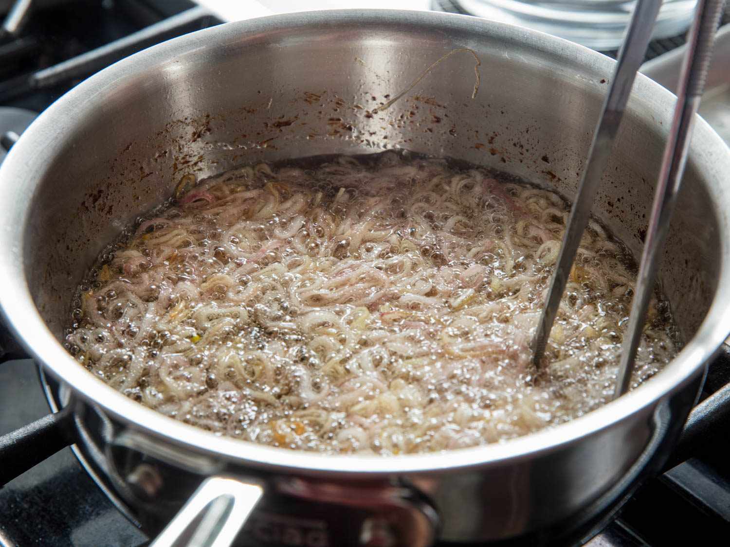 Stirring shallots as they fry to make sure they cook at an even rate.