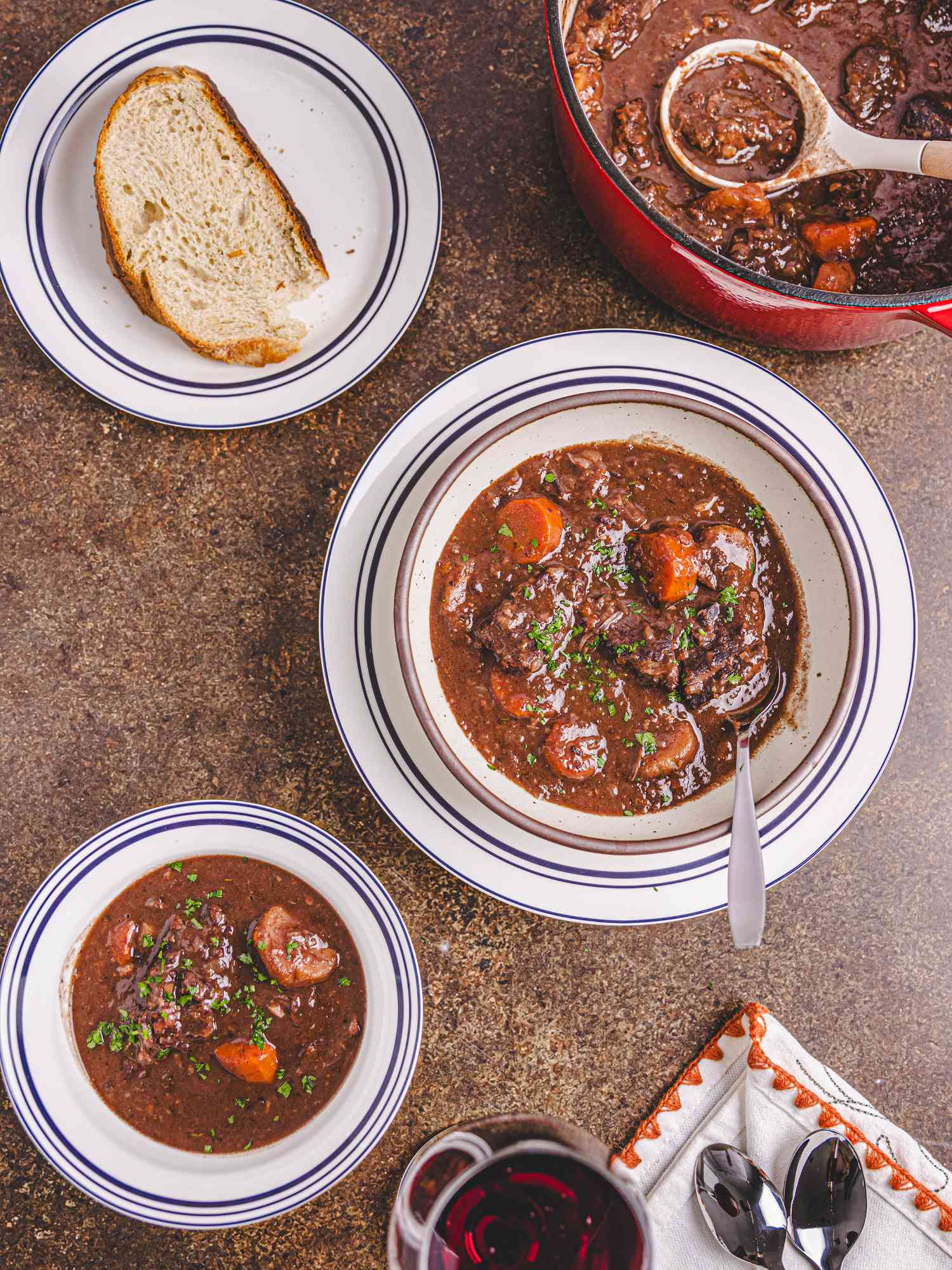 Gascon Beef Stew from above in a white bowl with a piece of bread on a small plate to the side and a red pot of stew 