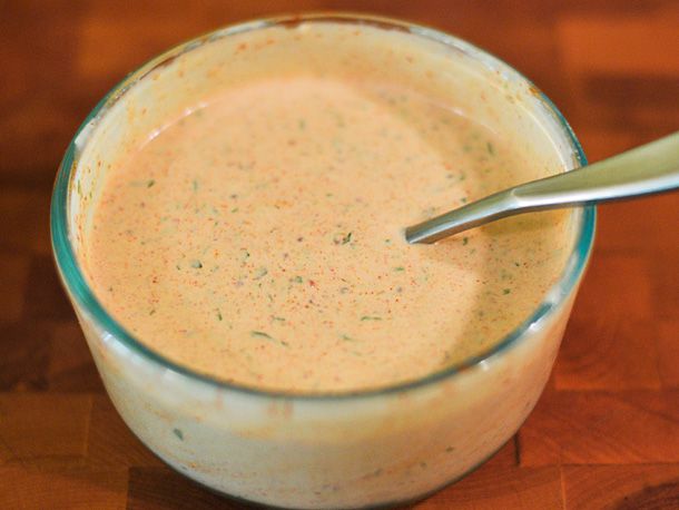 A bowl of finished remoulade sauce with a spoon in it on a wooden surface.