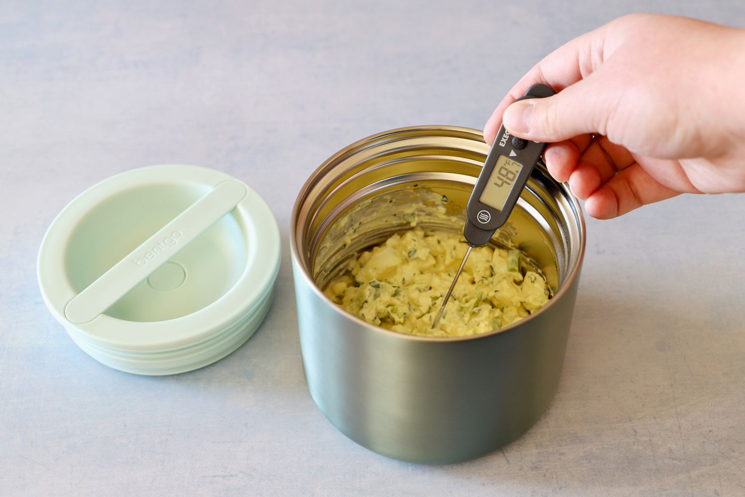 A hand taking the temperature of chilled egg salad in a food thermos