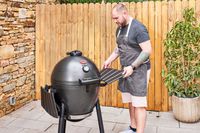 A person installs a shelf on the side of a Char-Griller E16620 Akorn Kamado Charcoal Grill