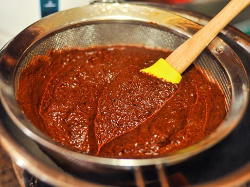A chile purée being strained through a strainer.