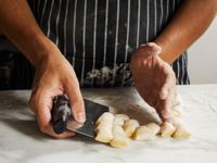 A person uses a bench scraper to lift up a pile of gnocchi