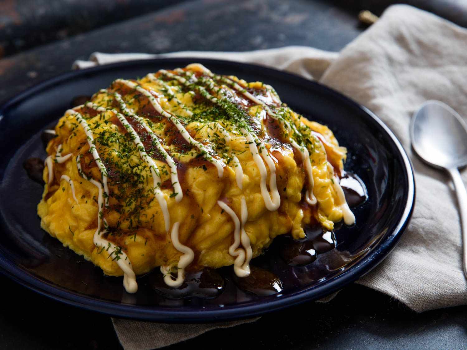 A moodily lit image of omurice, topped with aonori and squiggles of kewpie mayonnaise and okonomiyaki sauce.