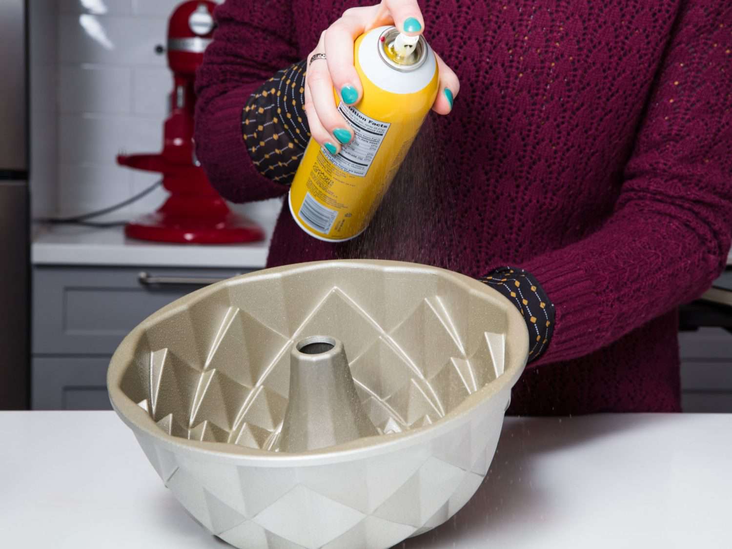 A person spraying cooking spray in a Nordicware bundt pan.