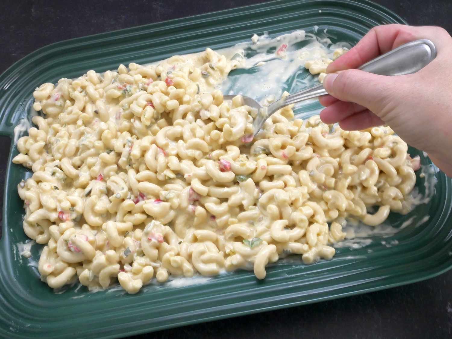 a hand scooping macaroni salad from the le creuset platter