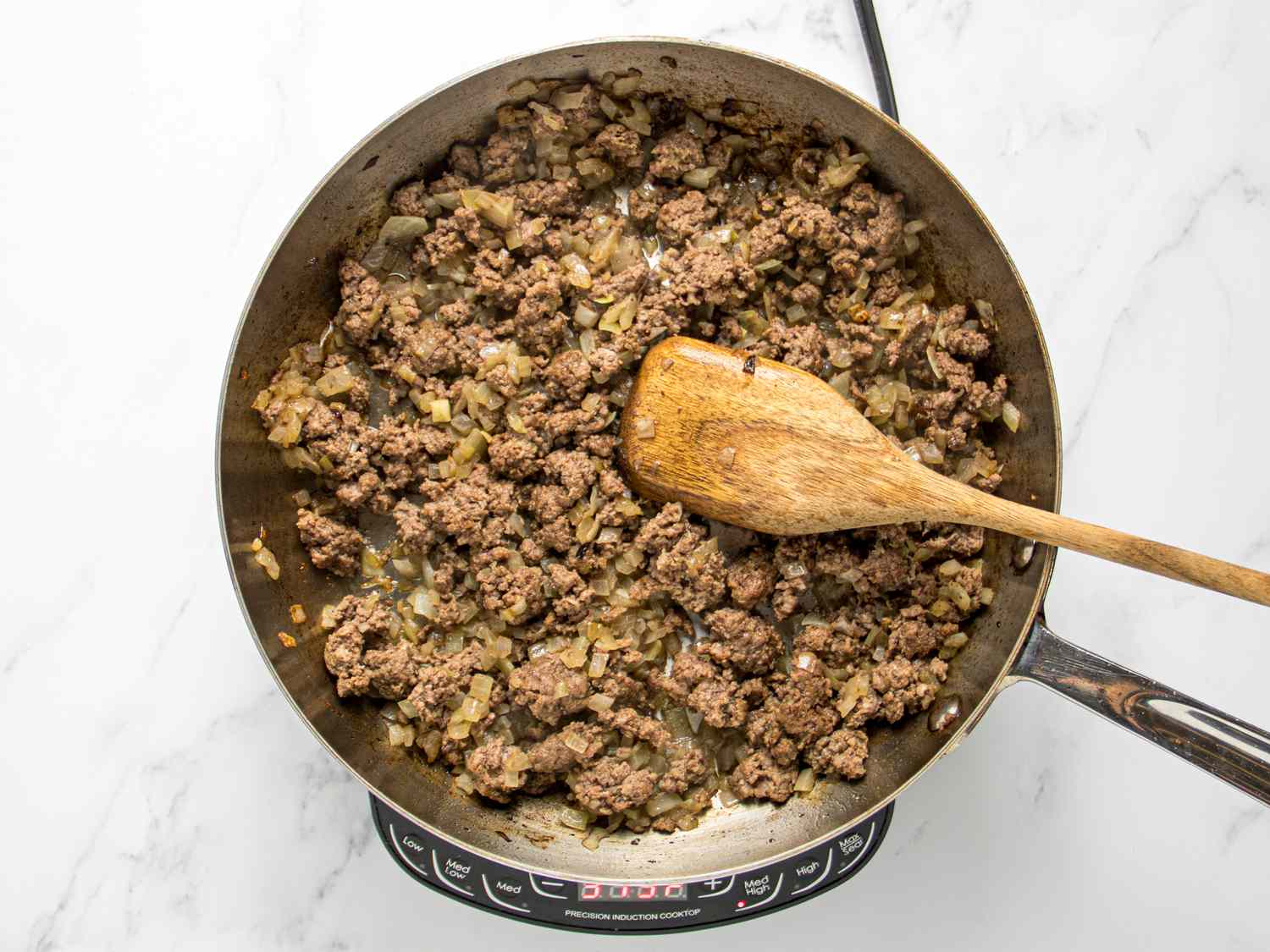 Breaking up ground beef and onion with a wooden spoon in a skillet. 