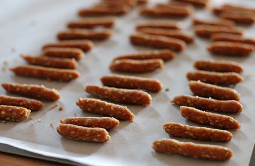 Hand-formed sesame dough rods on a parchment-lined sheet pan.