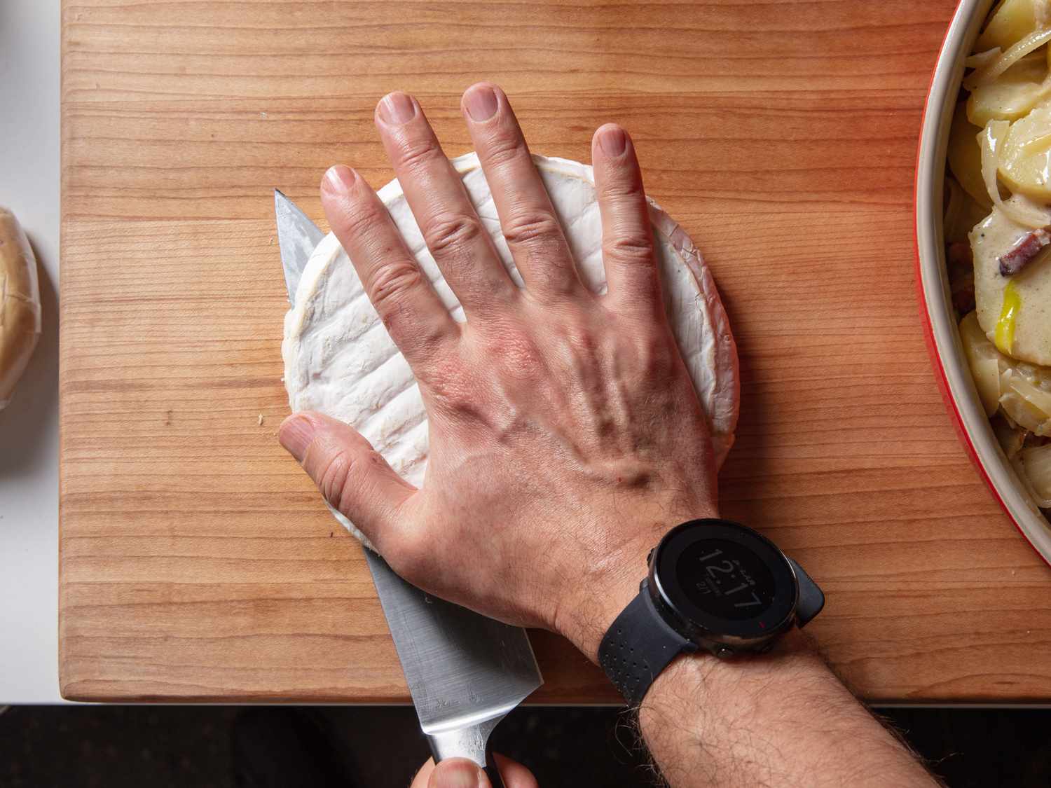 Cutting a wheel of cheese in half through the middle for tartiflette.