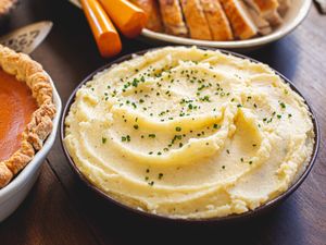 A bowl of mashed potatoes garnished with chives on a table with Thanksgiving dishes
