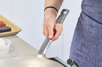 A person holds the handle on the Vollrath 12.5 Inch French Style Carbon Steel Fry Pan