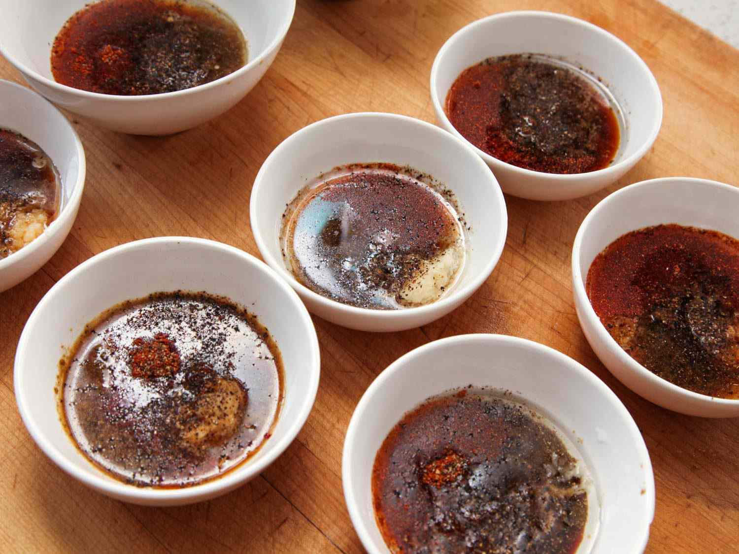 White bowls holding various marinade ingredients for fajitas, against a wooden cutting board.