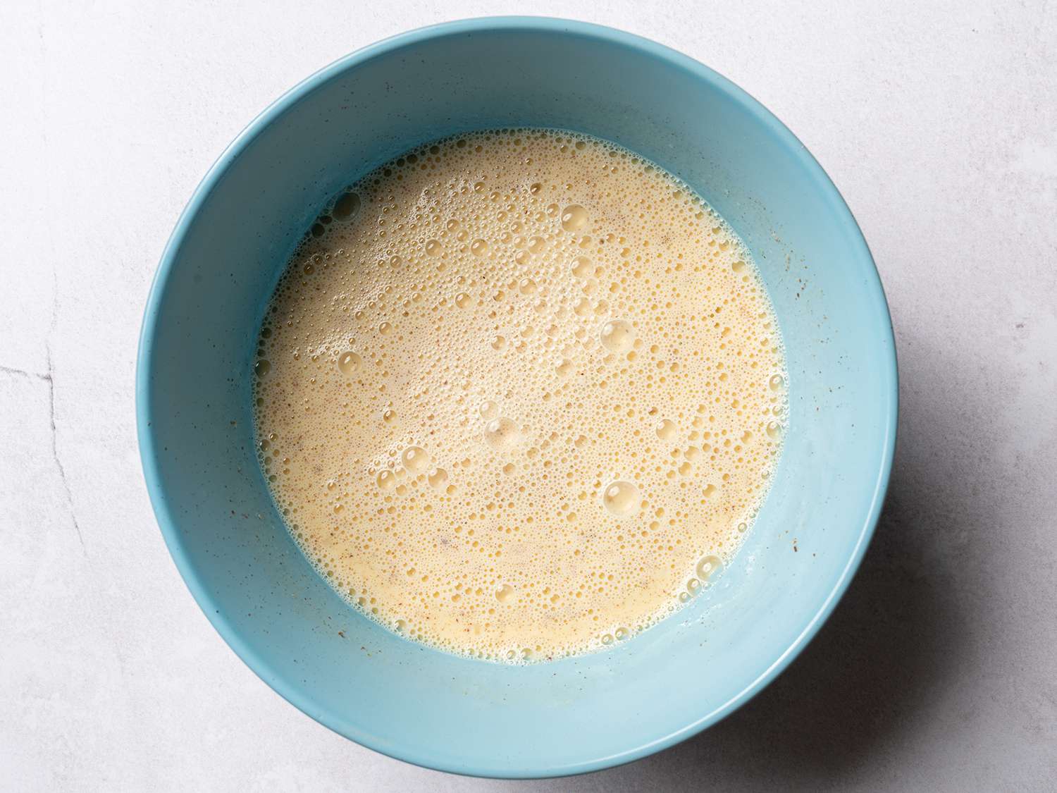 Overhead view of egg and milk mixture in a light blue bowl.