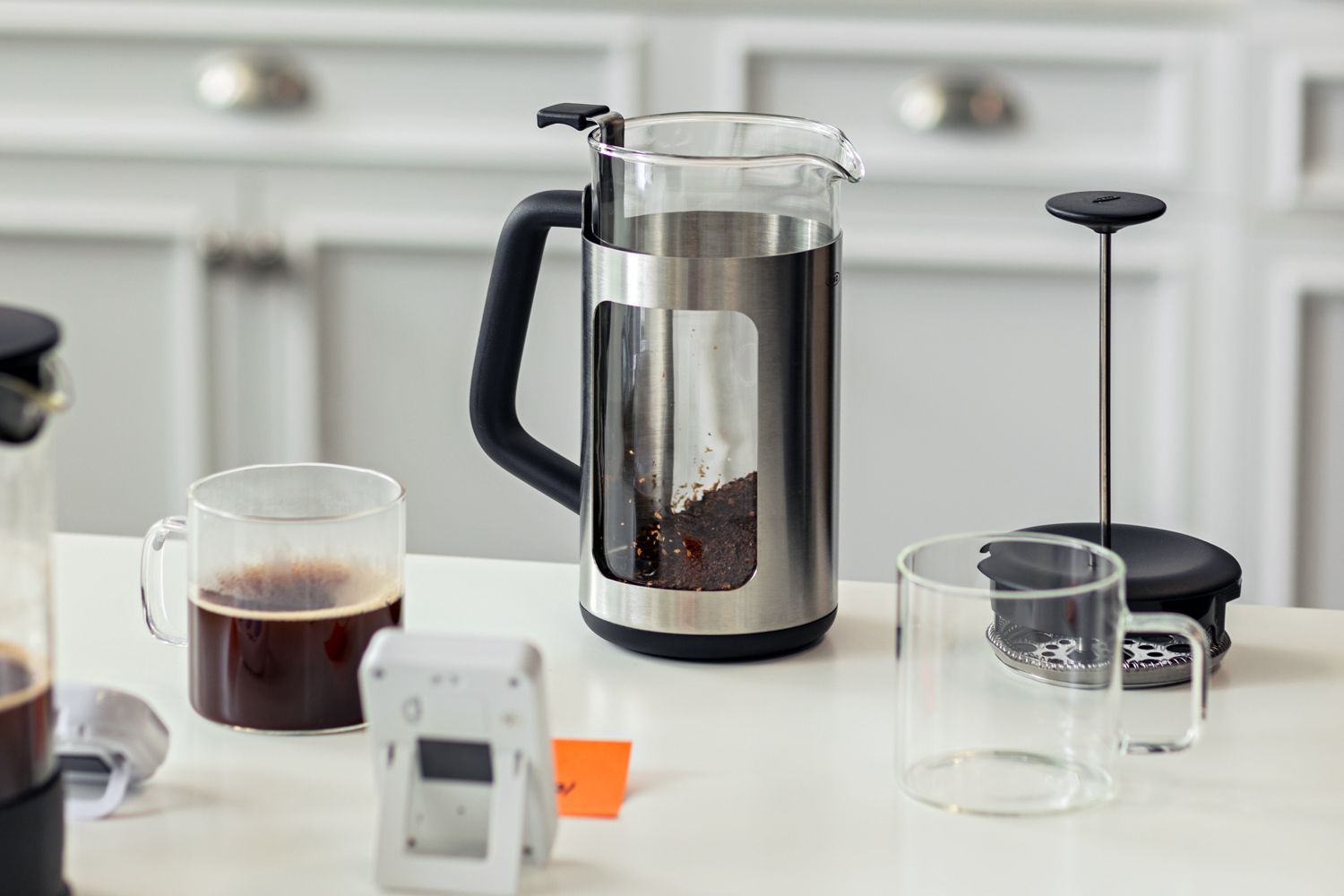 a French press coffee maker with a cup of coffee sitting beside it