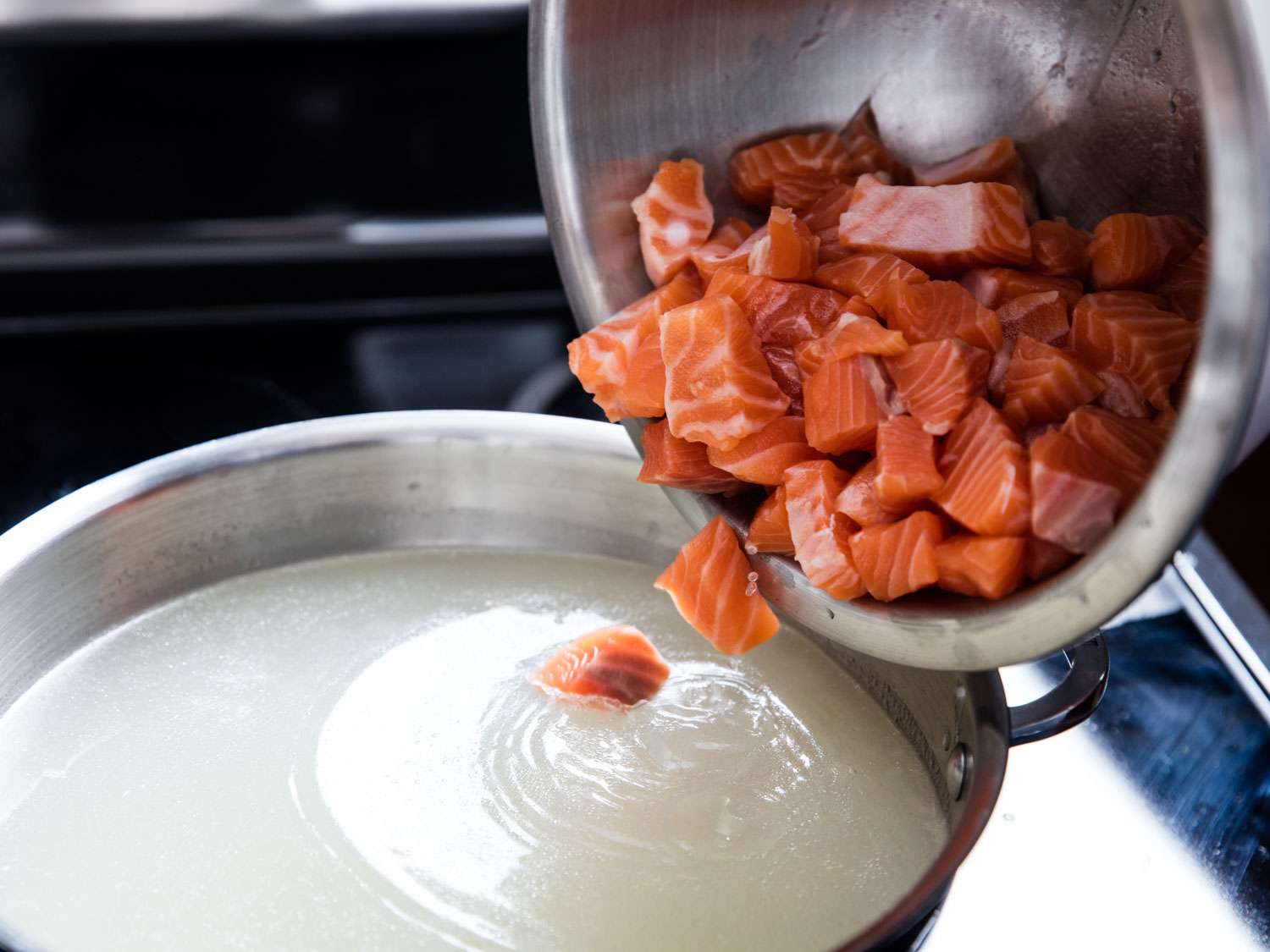 Tipping cubes of raw salmon into a pot of poaching water for rilletes.