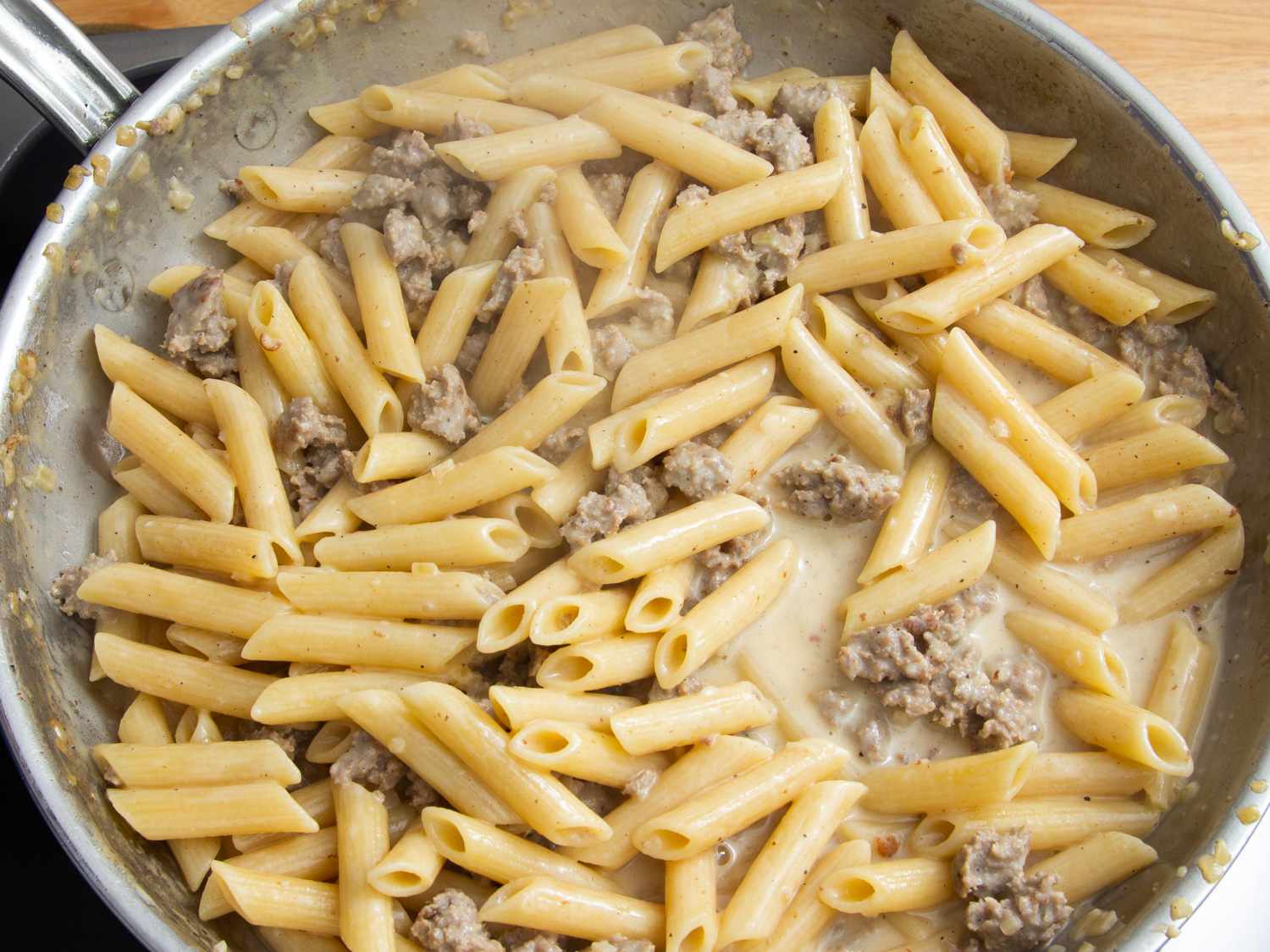 Penna and sausage cooking and mixing together in a skillet.