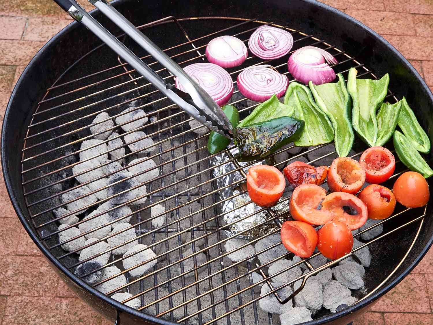 Vegetables including tomatoes, peppers, and onions being grilled over charcoal on a barbecue
