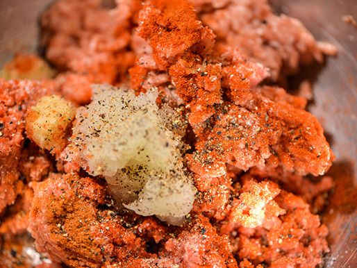 Grated onion, garlic, and spices on raw ground lamb and beef.