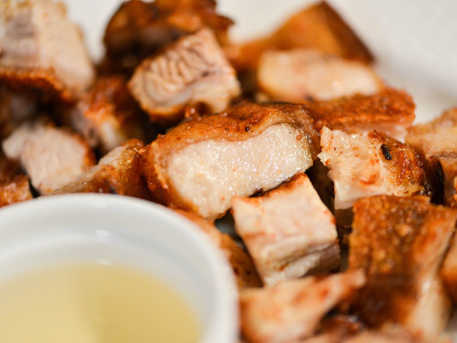 Cooked lechon kawali on a plate next to a small bowl of sauce. 