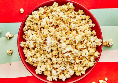 Red bowl full of Kettle corn on a red and green striped surface 