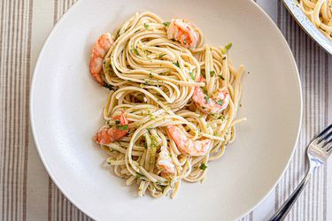 A plate with spaghetti and shrimp, garnished with herbs, placed on a table with a fork nearby