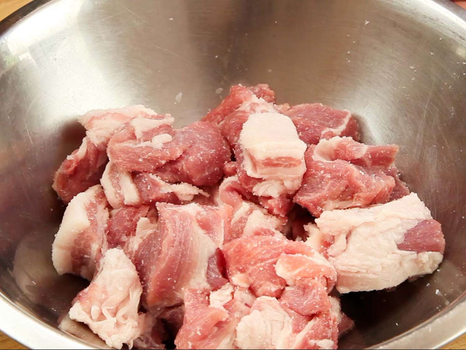 Raw pork chunks in a stainless steel bowl.