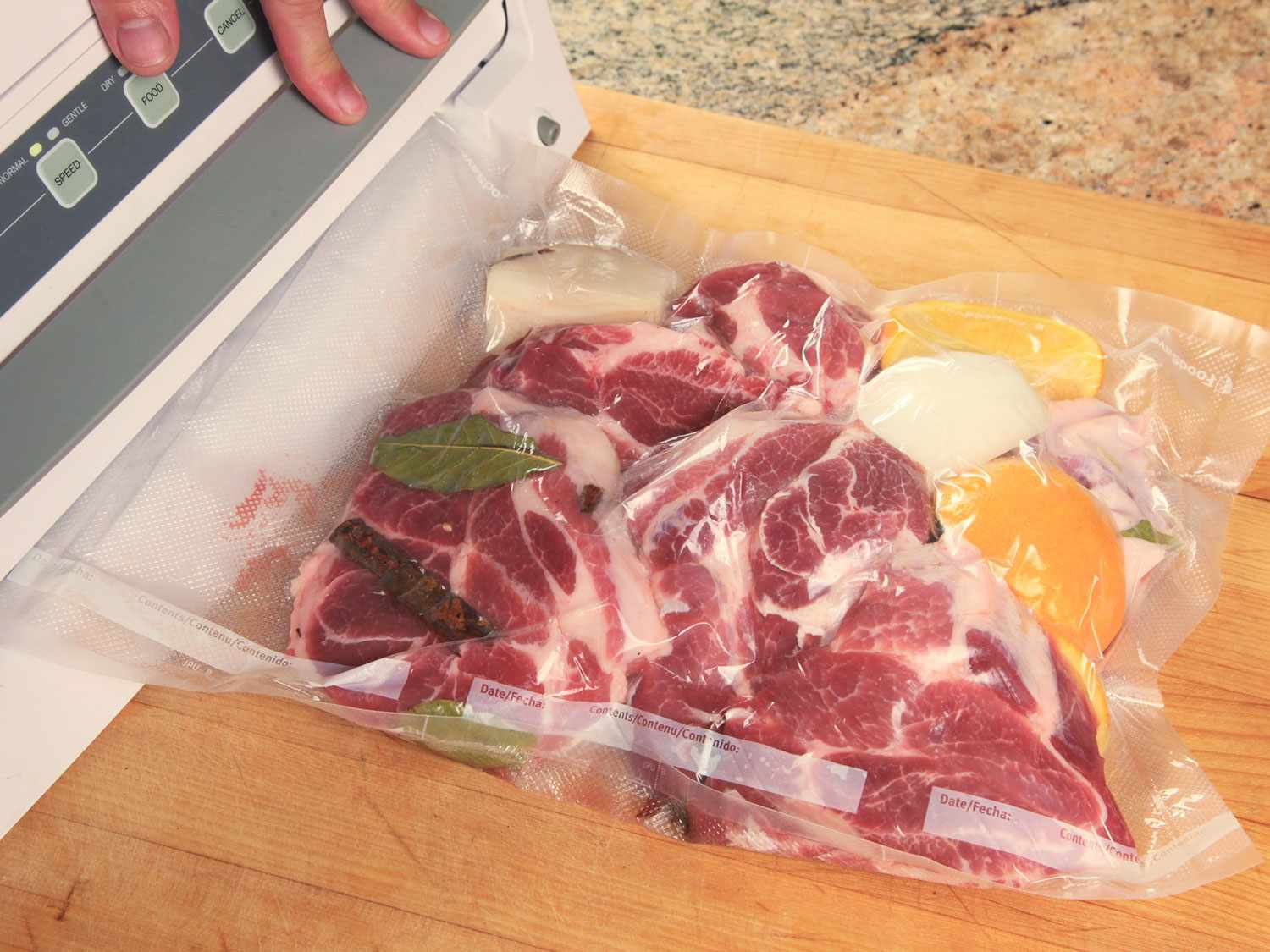 Sealing pork shoulder with bay leaves, cinnamon, onions, and oranges in a vacuum-seal bag before cooking sous vide for carnitas.