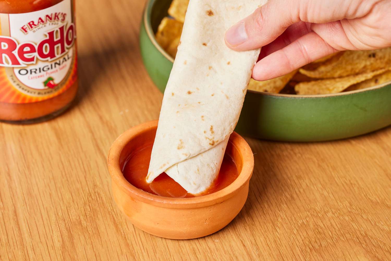 Person dipping tortilla into Frank's RedHot Original Cayenne Pepper Sauce