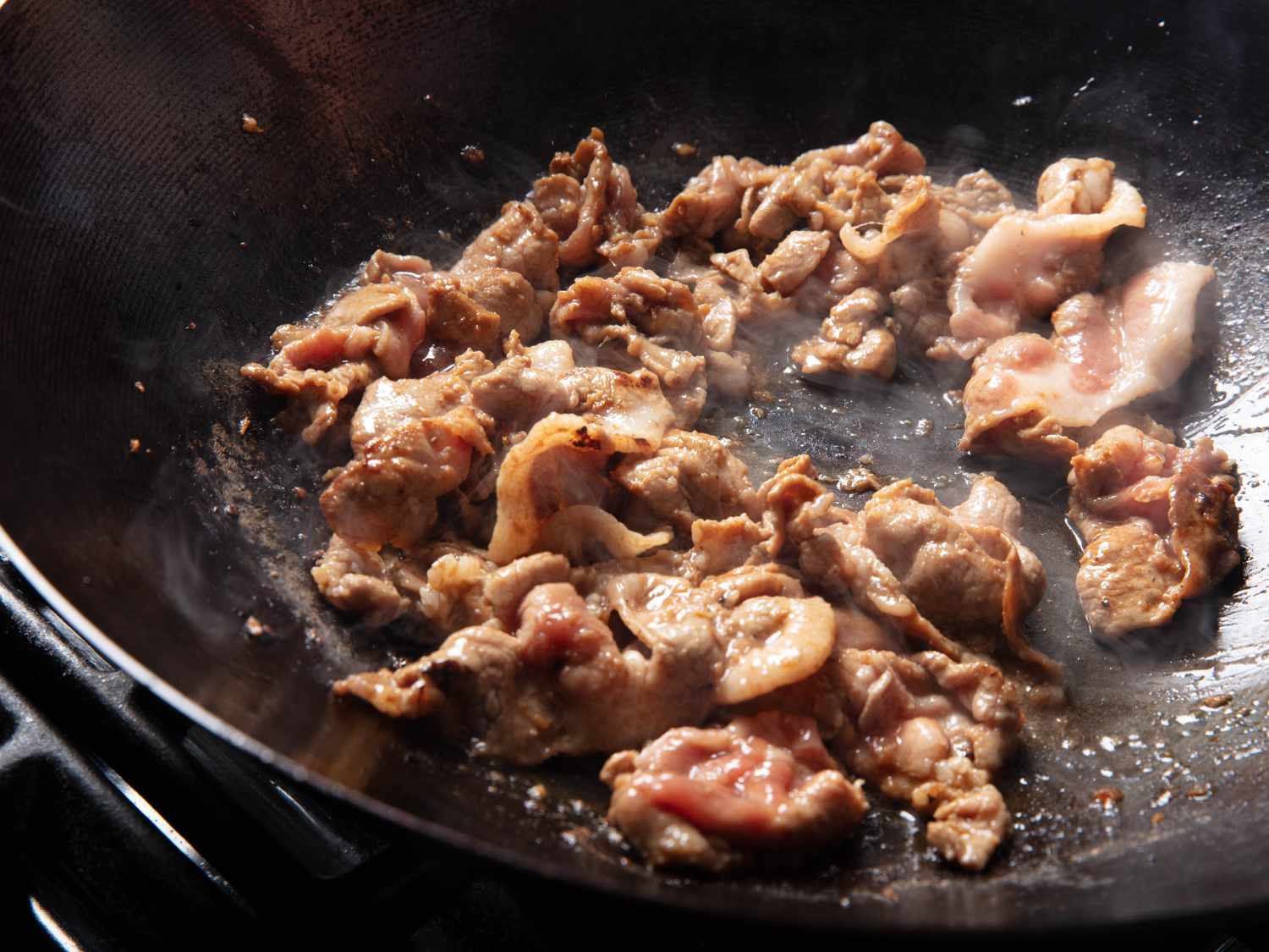 Thinly sliced, marinated pork cooking in a hot wok