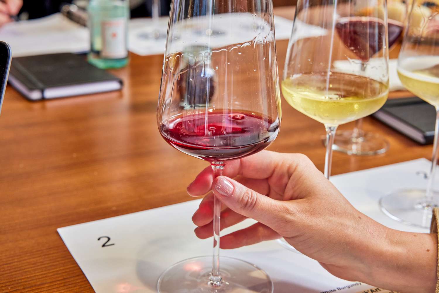 Hand holding one of two wine-filled Zalto Denk'Art Universal Hand-Blown Wine Glasses set on sheet of paper on wood table