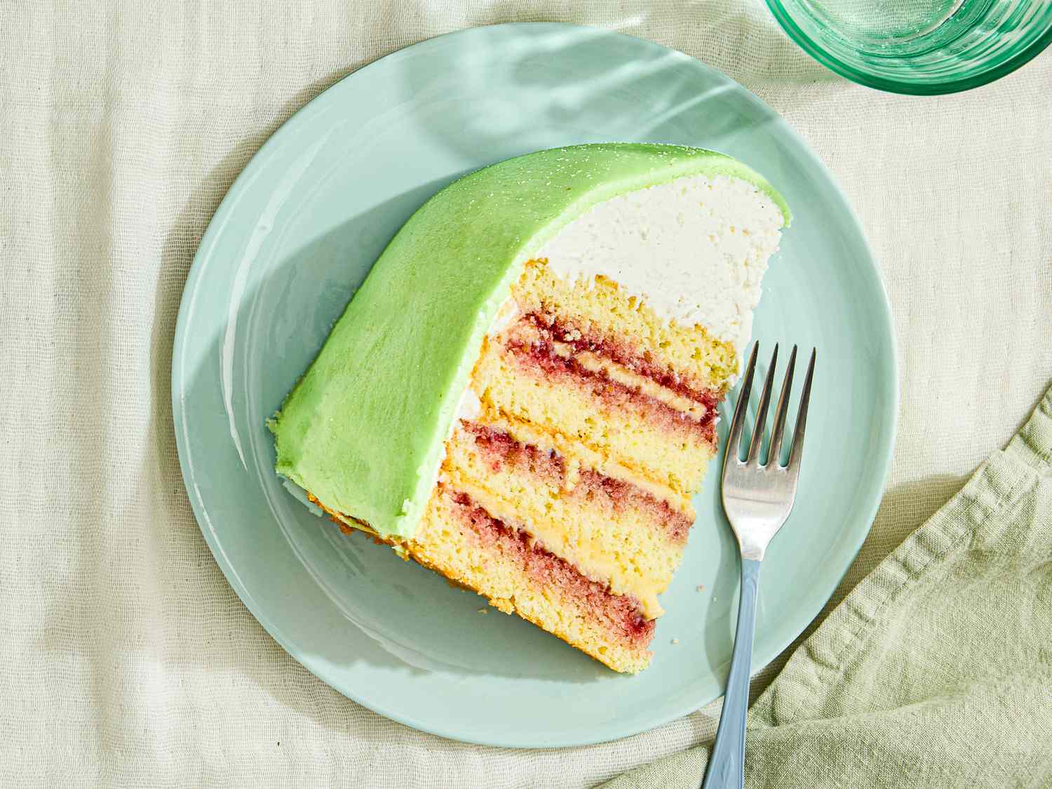 A slice of princess cake with layers of sponge jam cream and marzipan on a plate with a fork