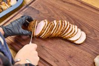 Sliced meat being cut on a Virginia Boys Kitchens Walnut Wood Cutting Board by a person wearing a glove