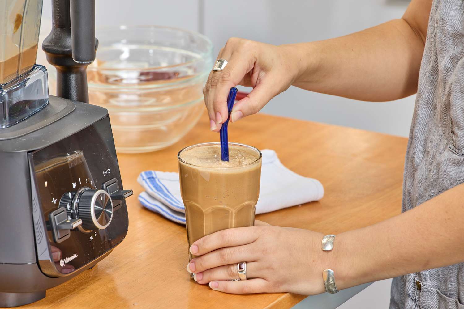 A hand adding a straw to a smoothie next to the Vitamix Ascent X2
