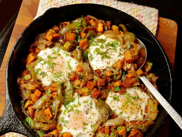 A cast iron skillet with sweet potato bell pepper hash topped with baked eggs.