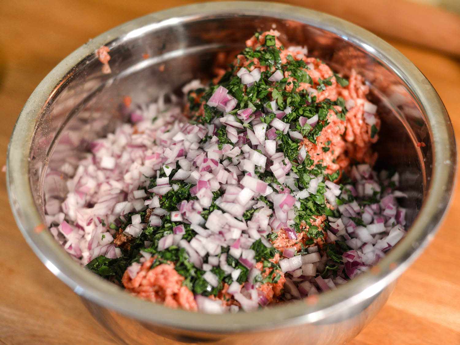 Onion, pepper, and parsley are added to the bowl of ground meat.