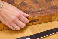 A hand holding the side handle of a Yes4All Teak Cutting Board