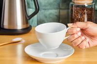 A person picking up a white porcelain cup off of a saucer.