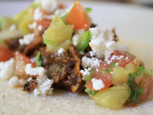 A close up view of a taco, filled with beef neck, cheese, and salsa. 