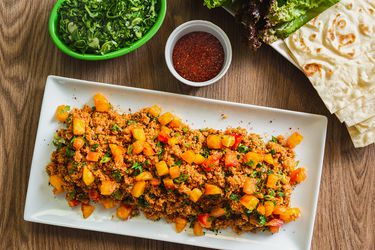Platter of eetch served with herb salad, lettuces, and lavash.