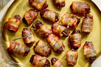 A plate of baconwrapped appetizers on a countertop served with small dishes and drink glasses