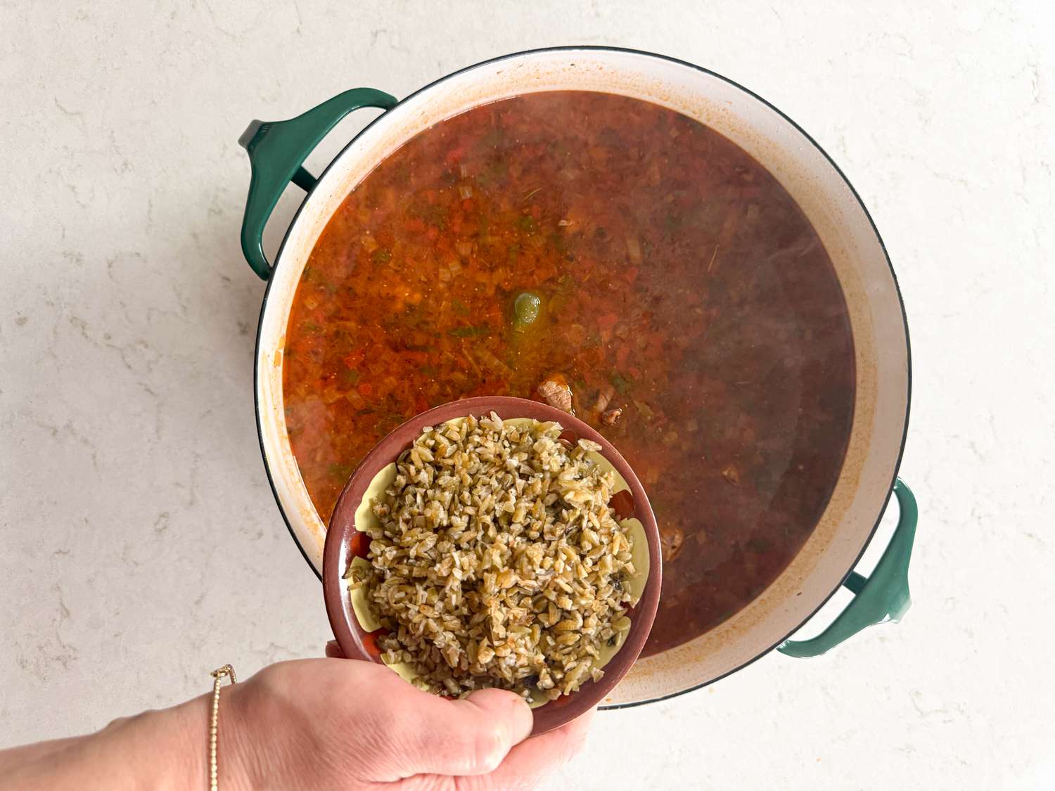 Adding freekeh into dutch oven on marble surface 