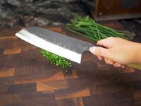 a person holding the sakai kikumori over a cutting board with minced chives